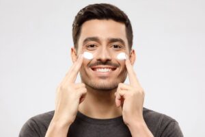 men is applying face cream on his both cheeks 
